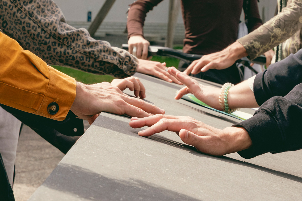 A concrete surface of the memorial is softly touched and caressed by the hands of six people. Every hand is touching this surface slightly differently, some are using their fingertips, others their palms.