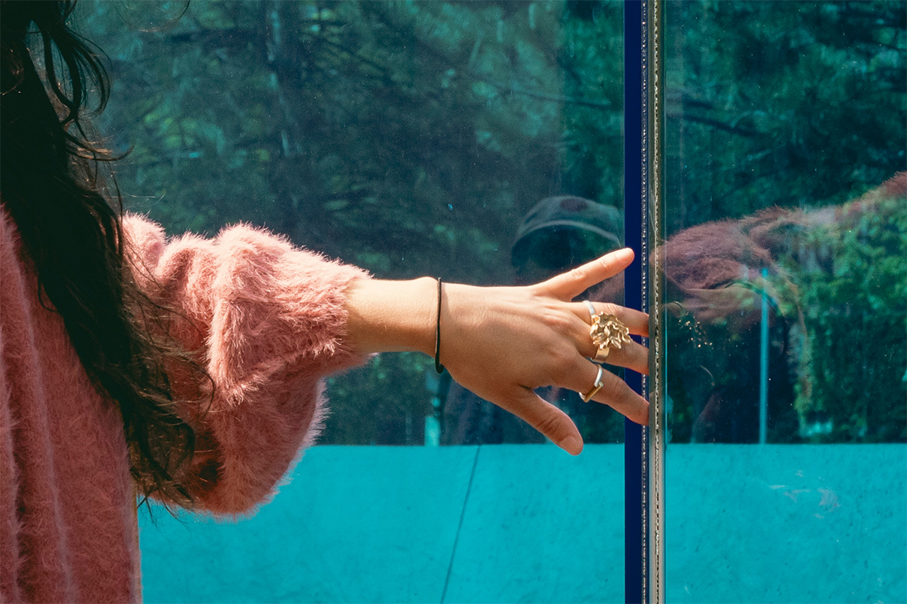 Between two blue sheets of glass, there is a gap through which the fingers of a person reach. The glass feels smooth.