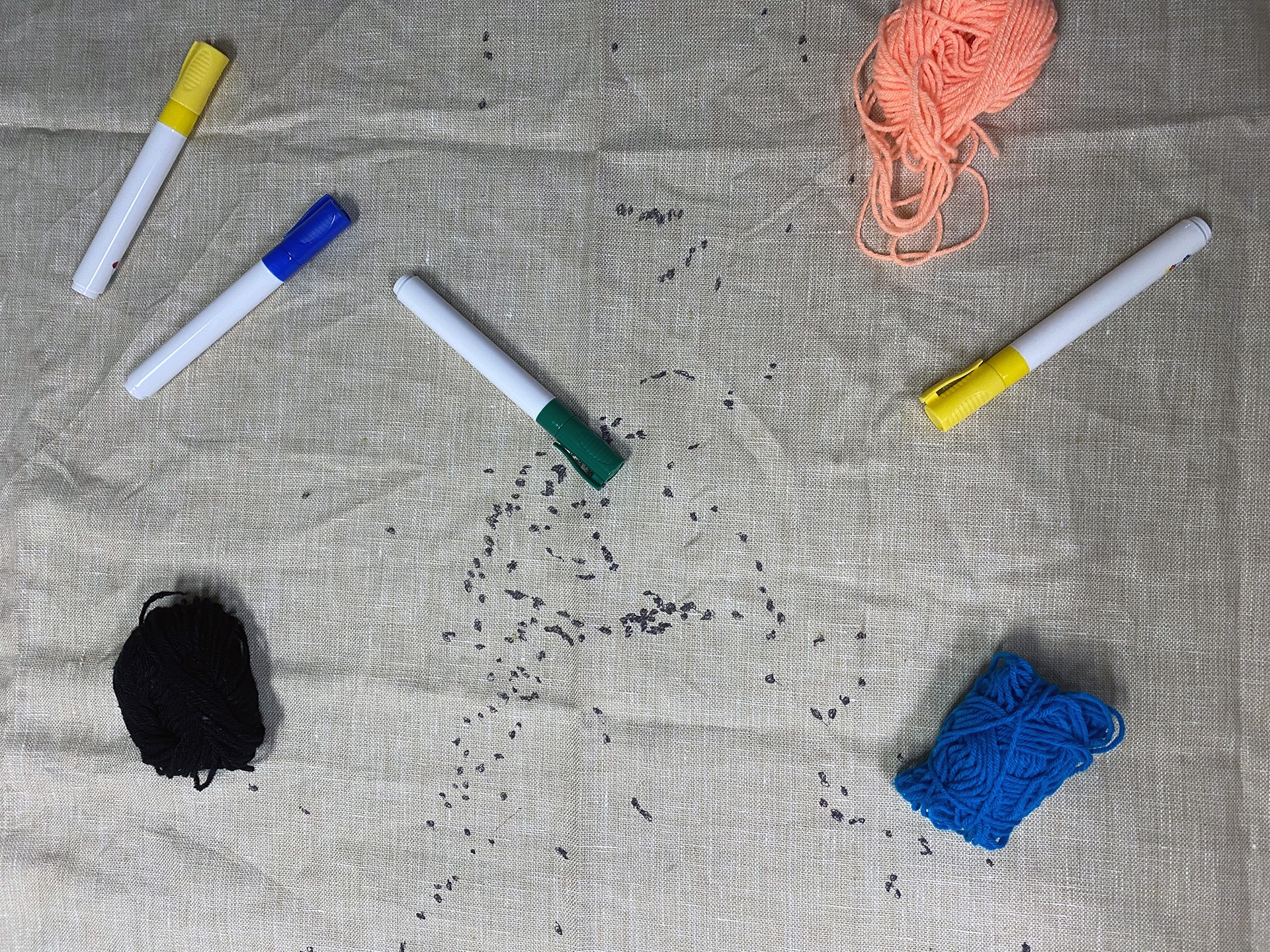 This photo shows a close up of a linen fabric that someone has painted black dots on top of. These dots form clusters, but it’s difficult to name any definite shape they form. The cap of a green pen enters the image from below. This photo was taken during a workshop in which participants later connected the dots, which represent internet landing stations, with pens and yarn.